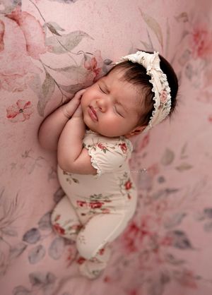 Newborn baby girl in pink floral outfit posed on a floral pink background, Brooklyn NYC newborn photographer.