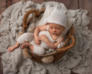 Newborn baby boy in white knitted outfit posed in rattan basket on a woody background, Brooklyn NYC newborn photographer.