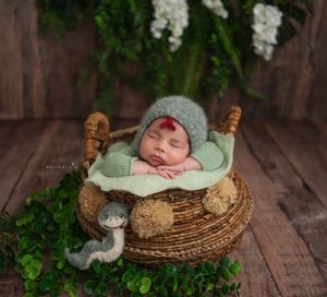 Newborn baby in green knit outfit sleeping in basket with greenery, Brooklyn NYC newborn photography.