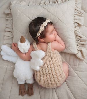 Newborn baby wearing beige knit outfit and headband, lying on textured blanket holding white stuffed toy, Brooklyn NYC baby portraits.