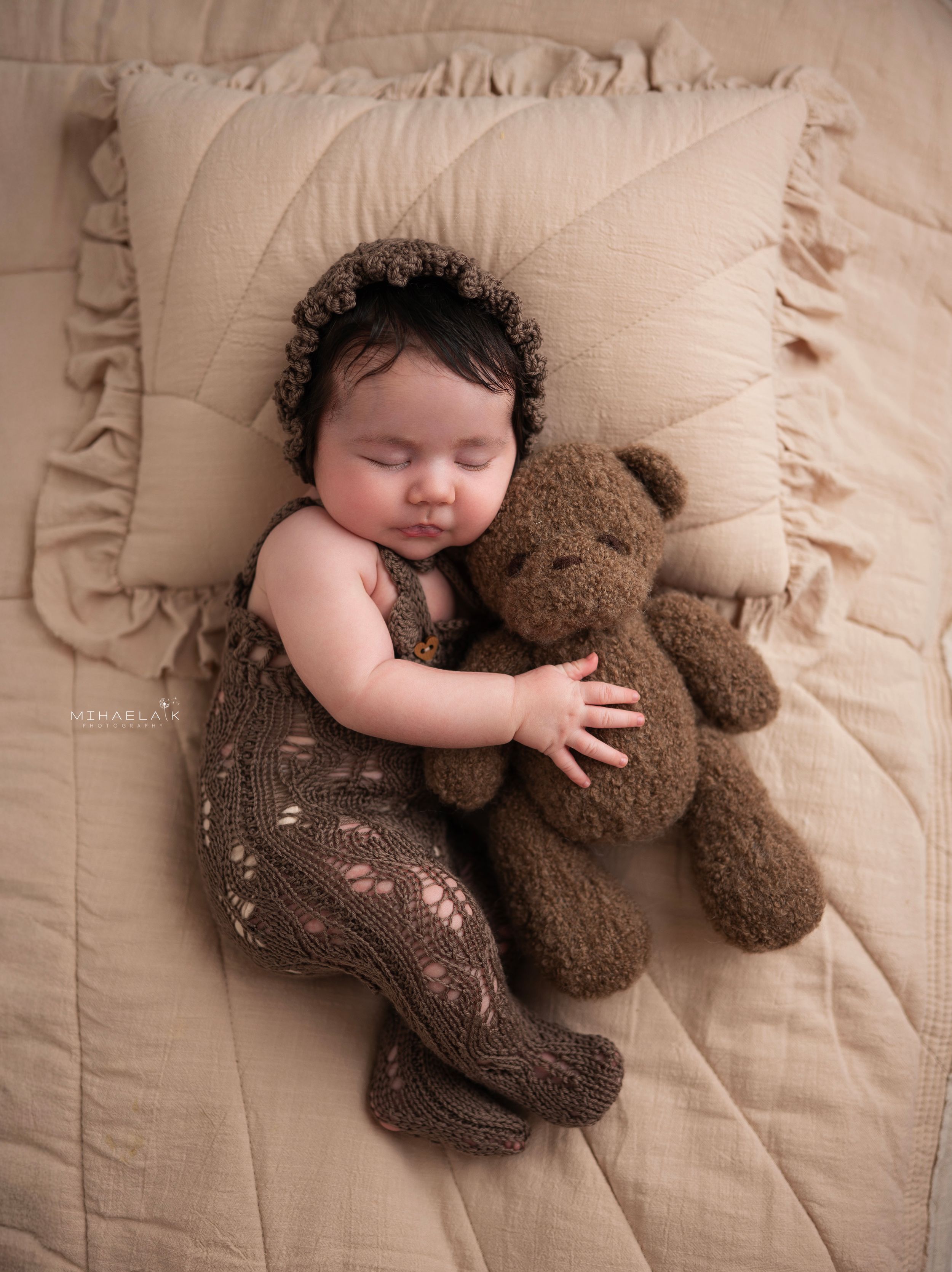 Newborn baby in brown knit romper and  bonnet  holding stuffed bear, Brooklyn NYC baby photography.