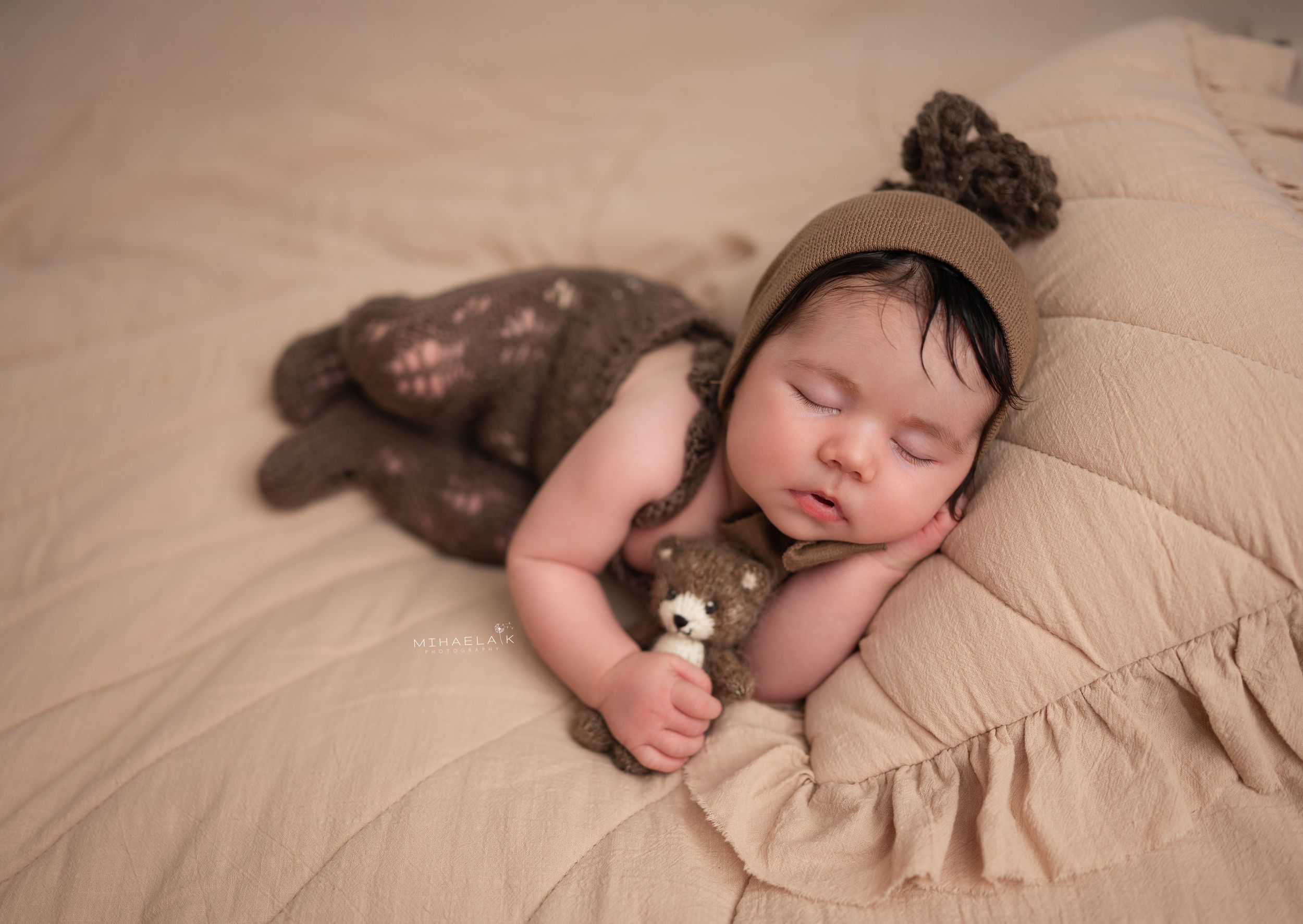 Newborn baby in brown knit romper and  bonnet  holding stuffed bear, Brooklyn NYC baby photography.
