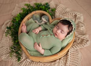 Newborn baby in green knit outfit sleeping in heart-shaped bowl with greenery, Brooklyn NYC newborn photography.