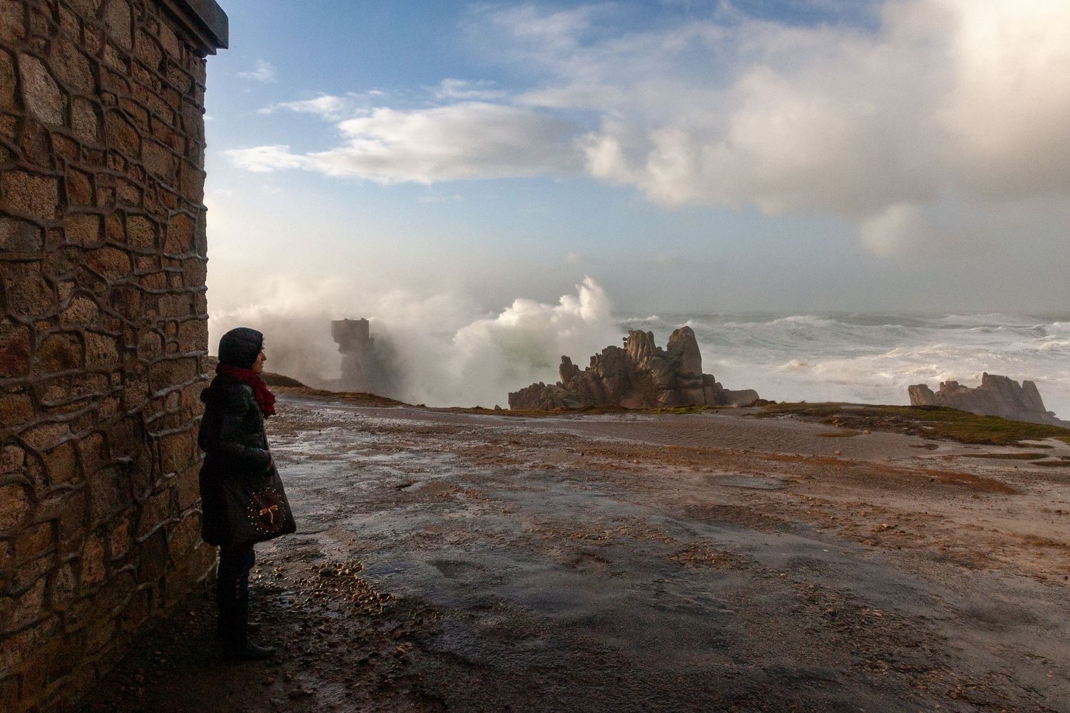 Person observes powerful ocean waves crashing against rocky cliffs in dramatic stormy weather.