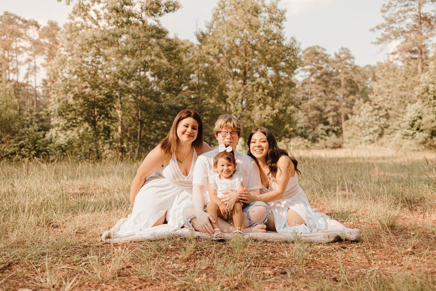A group sits together on a blanket for an outdoor photo session in a grassy field.