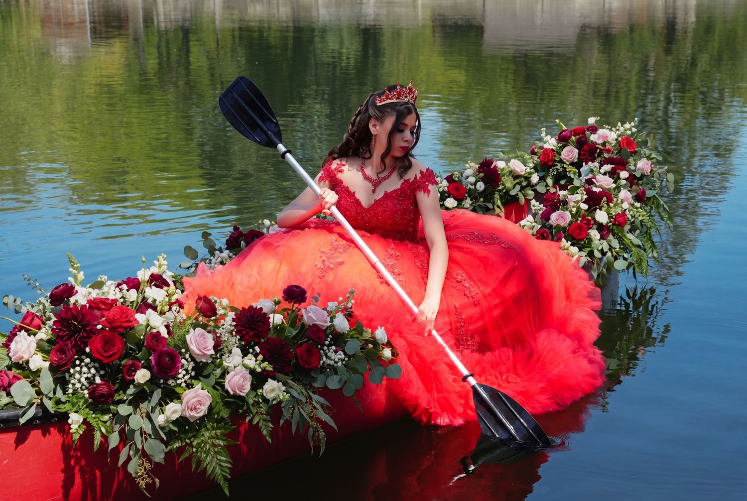 A woman in a flowing pink ball gown poses near stone columns in a lush green garden.