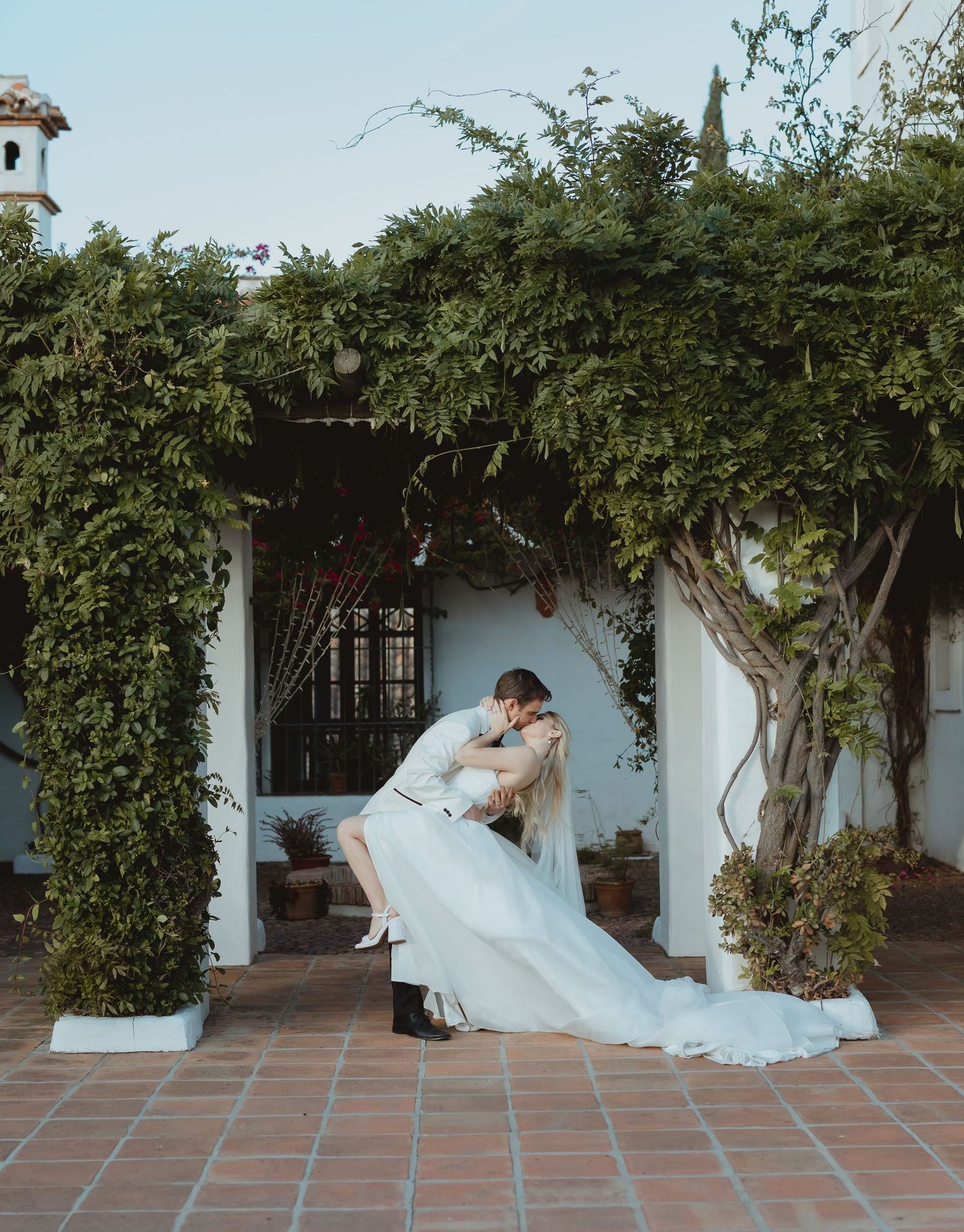 A romantic wedding photo sequence showing a couple embracing on a Spanish-style terrace with white walls and climbing vines.