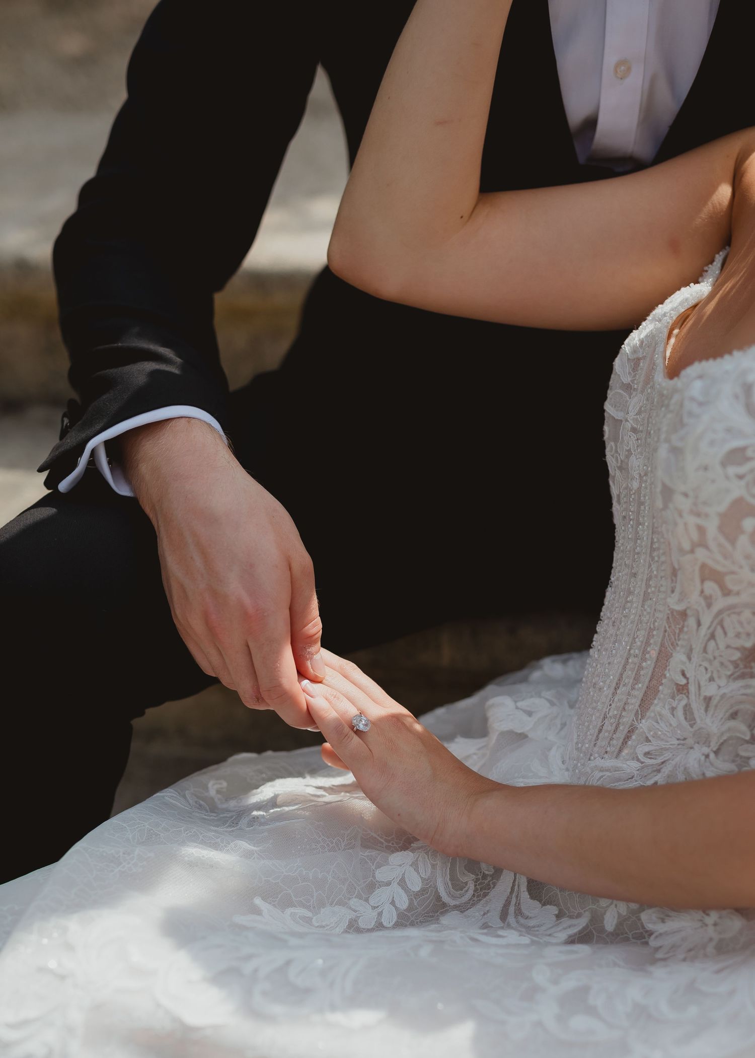 A close-up of hands adjusting a delicate white lace wedding dress train against a dark background.