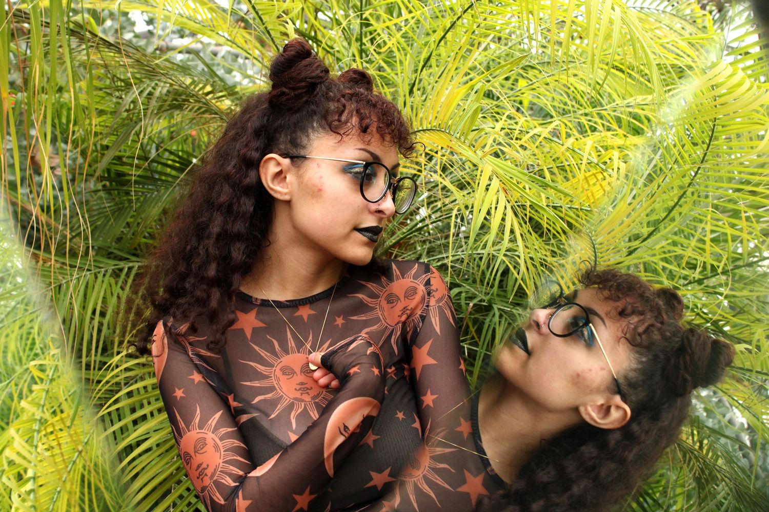 portrait of a young woman in front of palm leaves facing her reflection