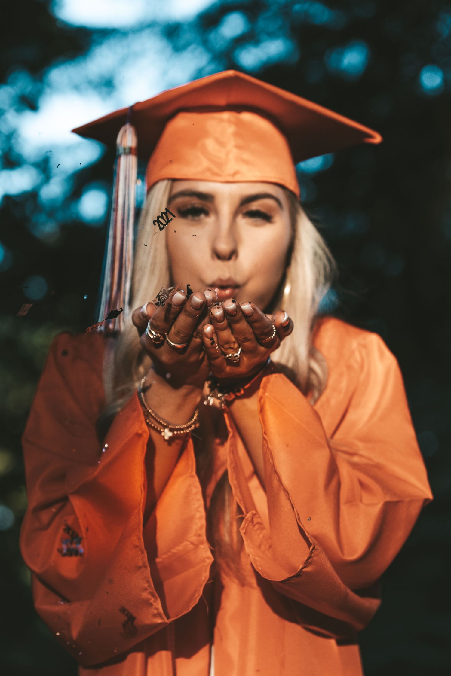Person in orange jacket blowing glitter or sparkles in artistic outdoor portrait.