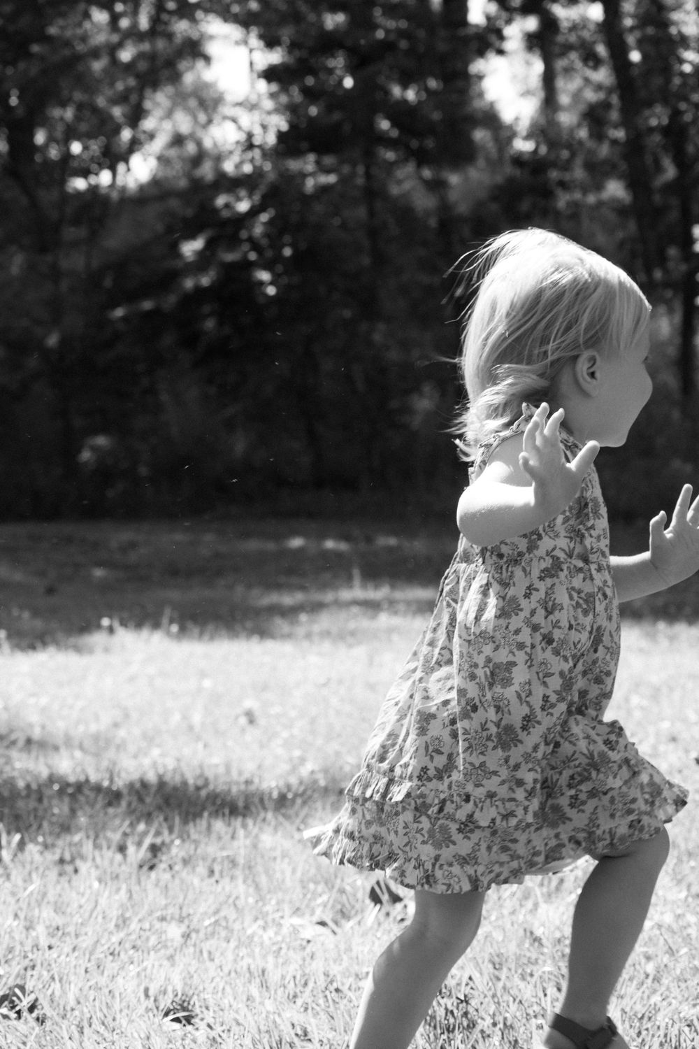 Black and white series of toddler running through grass in summer dress.