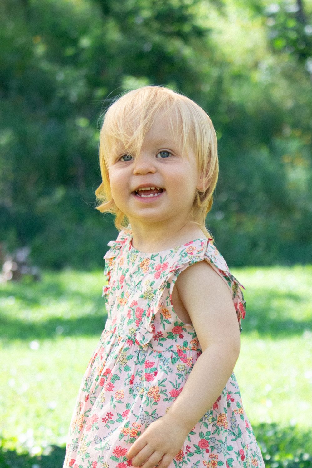 Smiling toddler in floral sundress enjoying a sunny day outdoors.