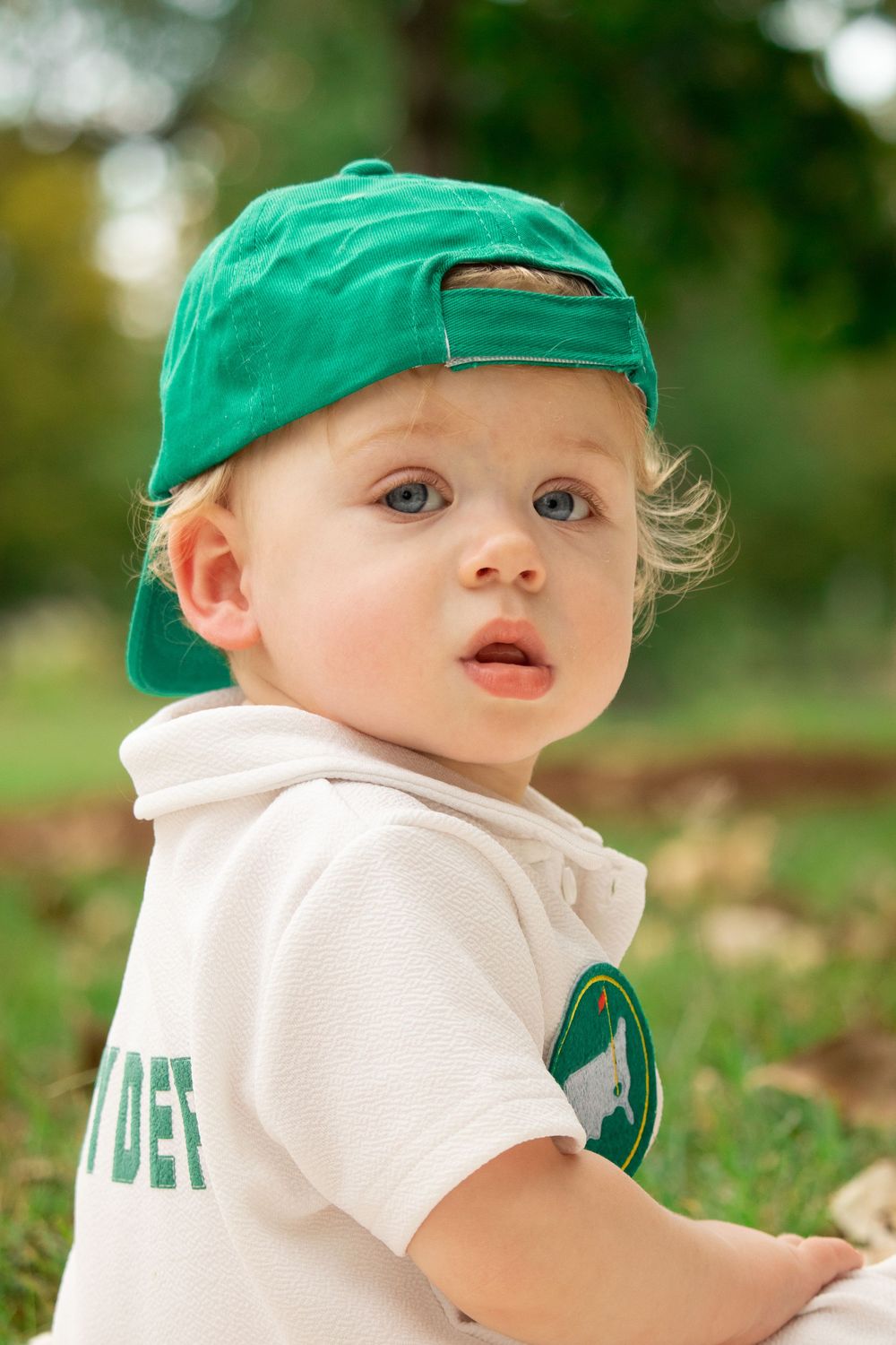 A young child wearing a green baseball cap smiles while playing outdoors.