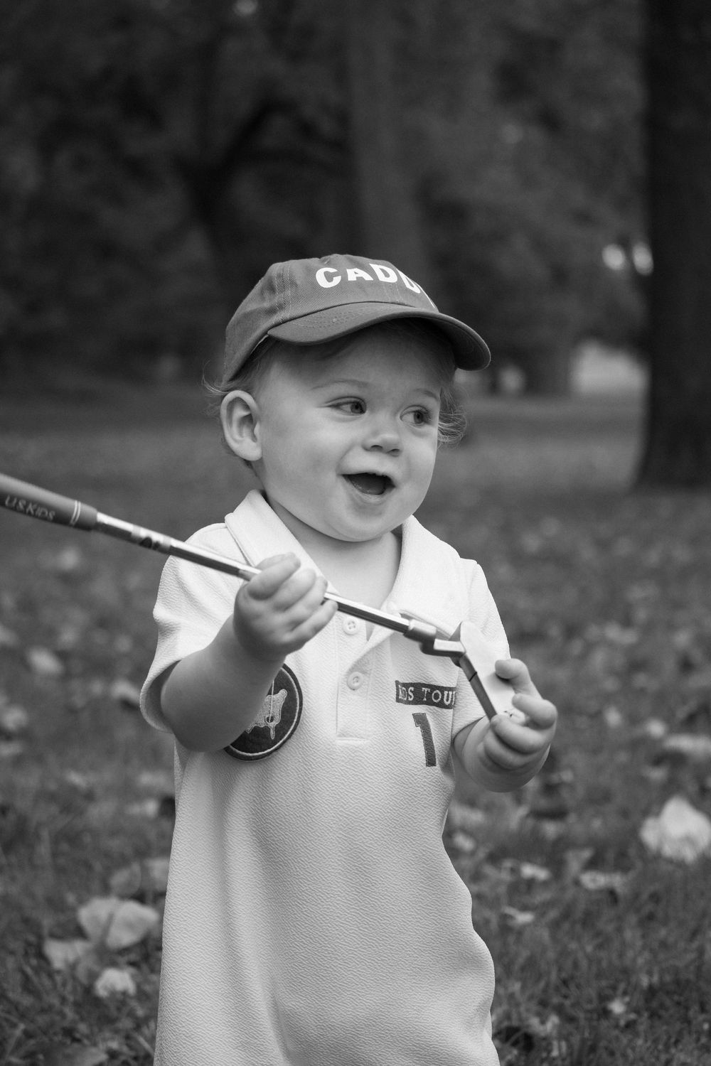 A happy toddler in a baseball cap plays outdoors in black and white.