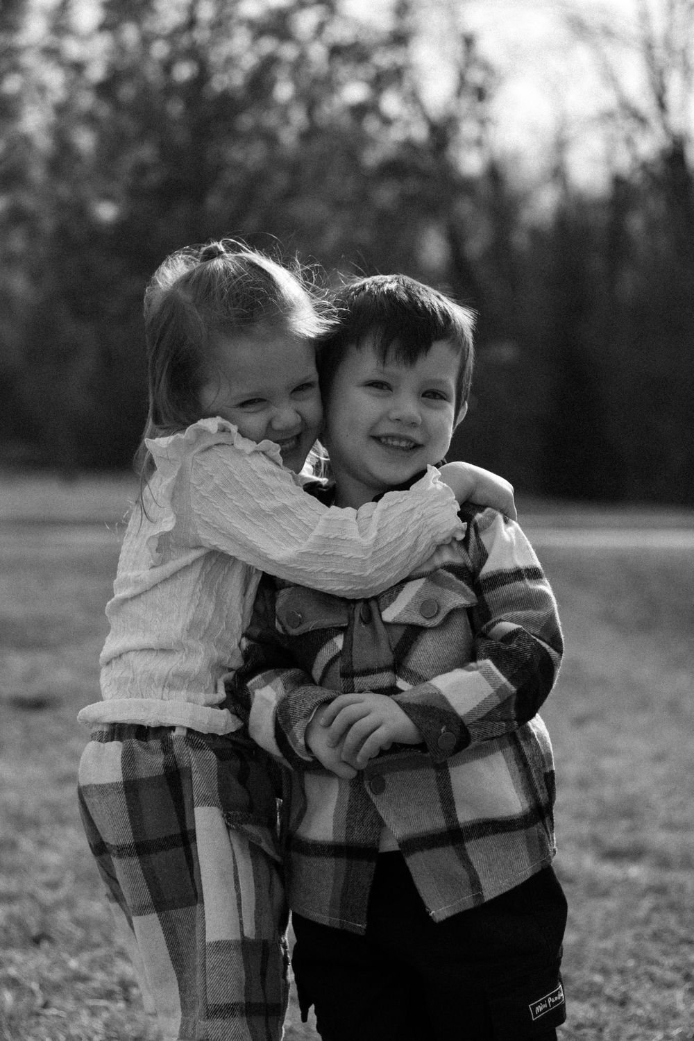 Black and white photography of children embracing in matching outfits.