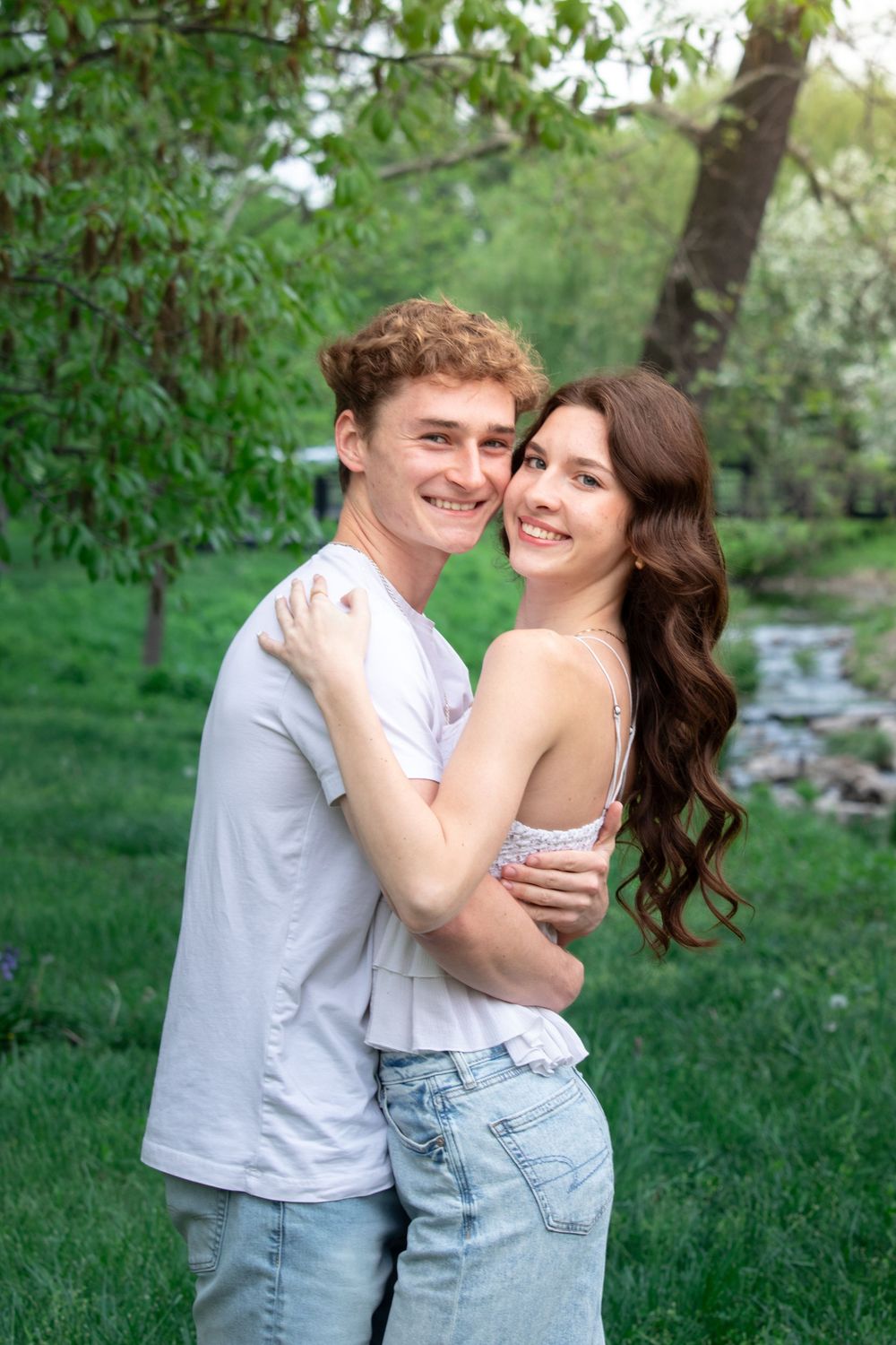 Couple embracing and laughing together in a green spring garden setting.