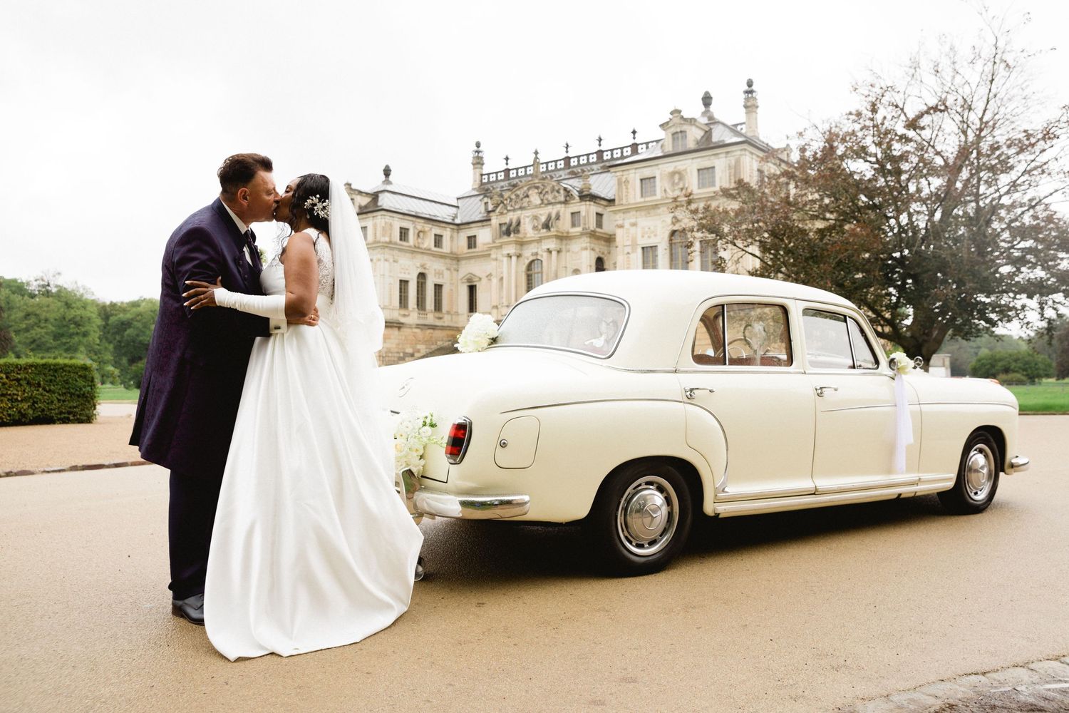 A classic cream-colored vintage car parked outside a grand estate on a wedding day. Organized wedding by MyCastleWedding | Dresden