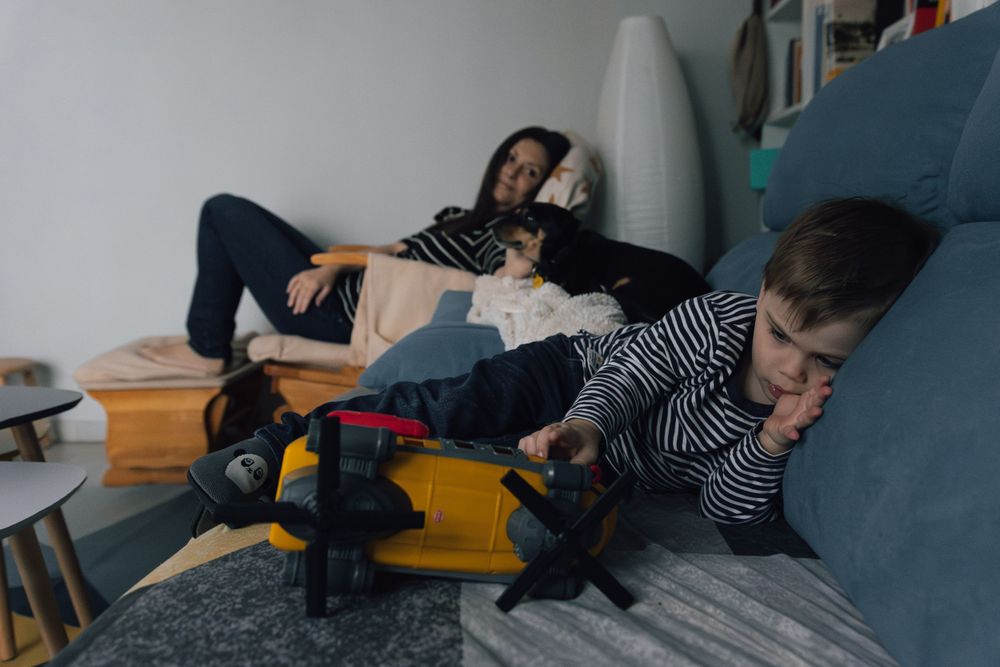 Two figures resting on a blue couch with toys scattered around. Photographe de famille fotógrafa de familia sevilla fotógrafo de la vida rea