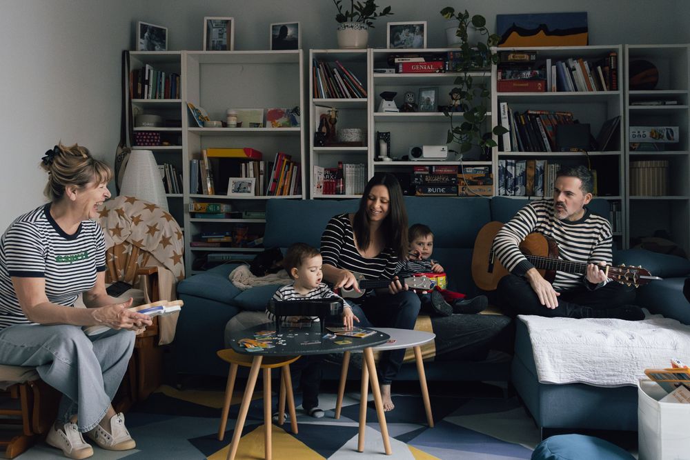 Group gathered in living room with guitars and bookshelves in background. Photographe de famille fotógrafa de familia sevilla fotógrafo de l