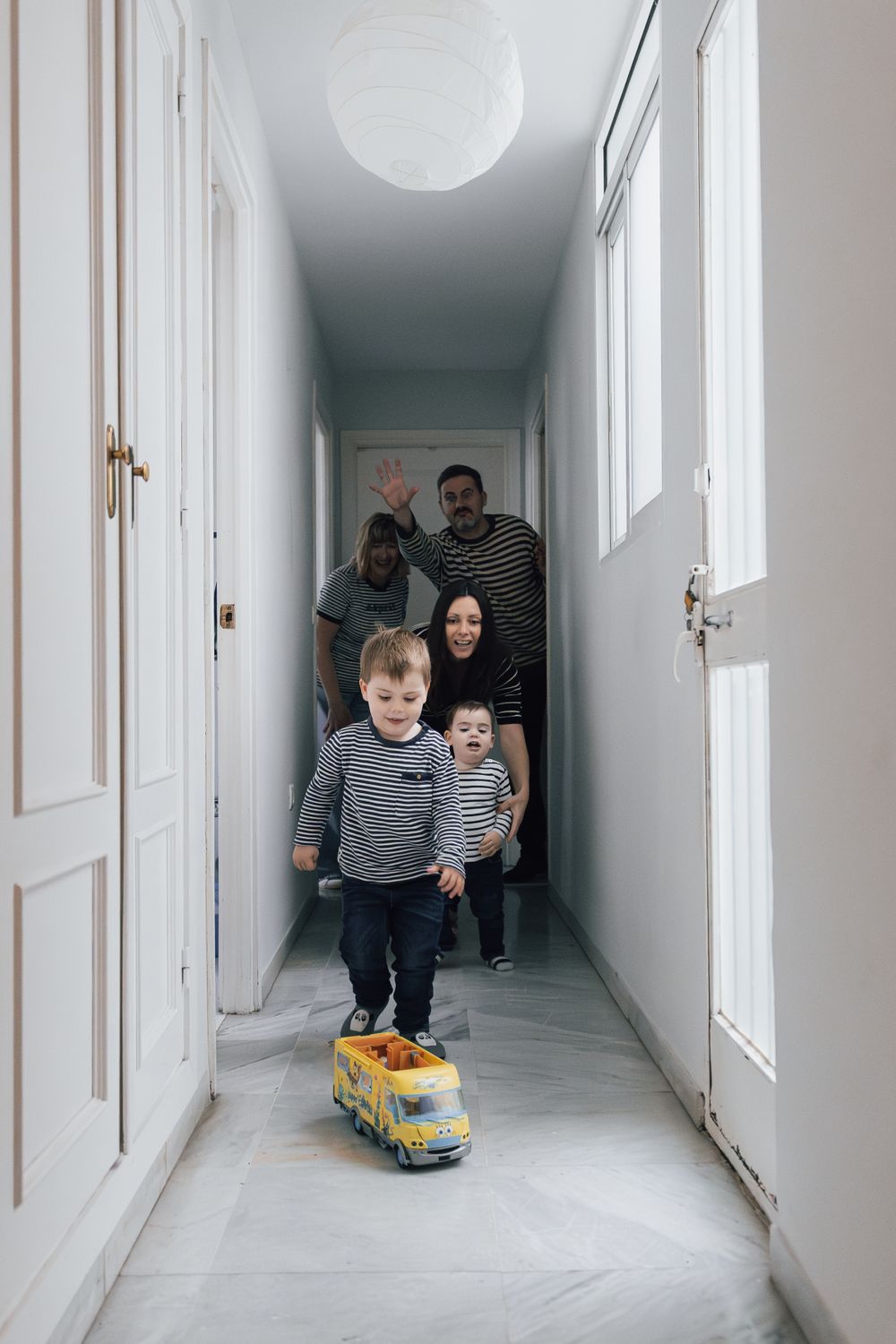 Family following behind toy truck in narrow white hallway. Photographe de famille fotógrafa de familia sevilla fotógrafo de la vida real