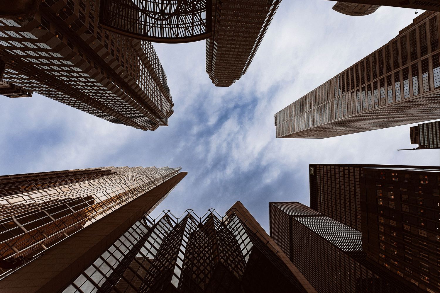 Looking up at towering skyscrapers from street level with dramatic perspective against blue sky.