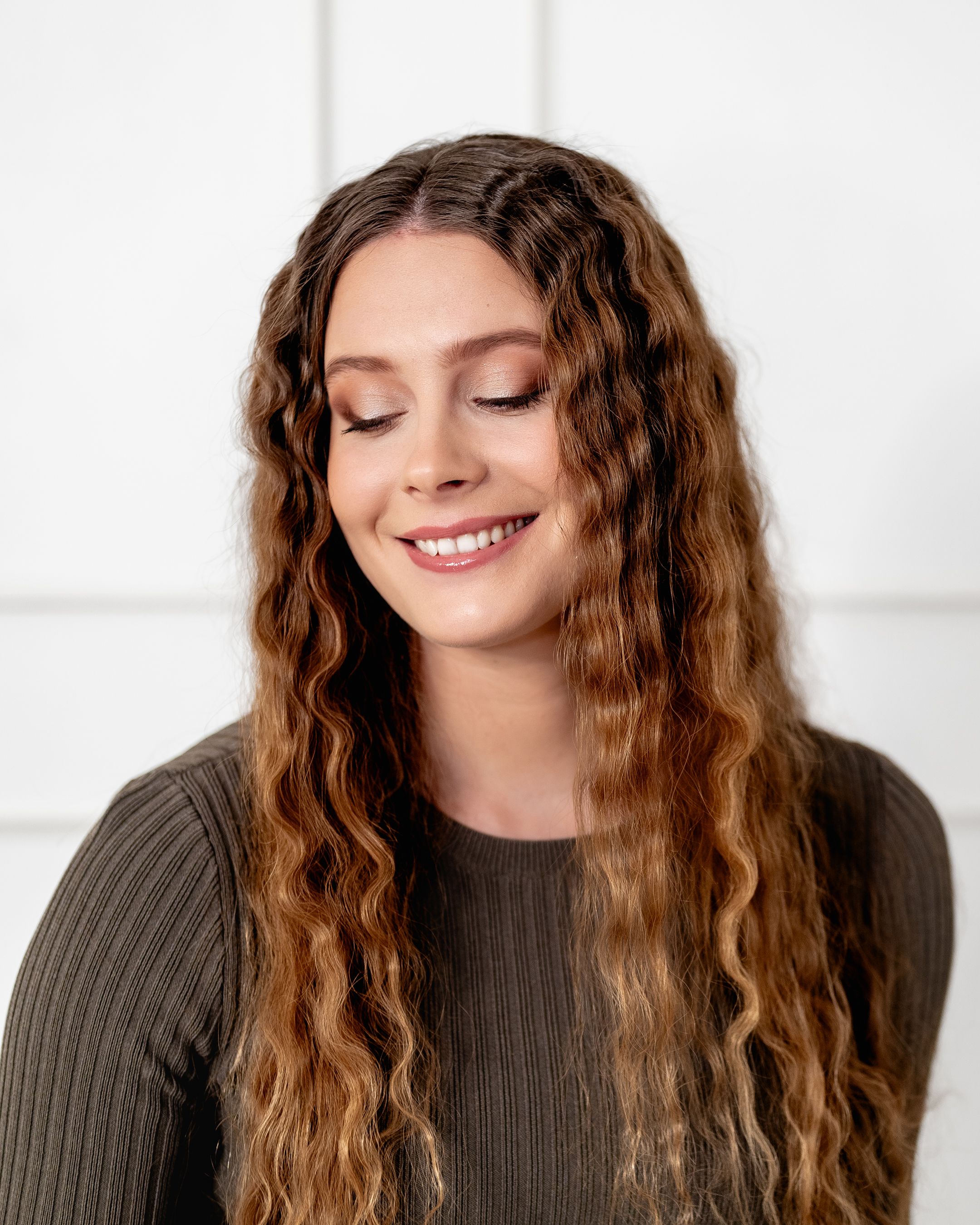Professional portrait featuring long wavy brown hair and natural makeup against white background.