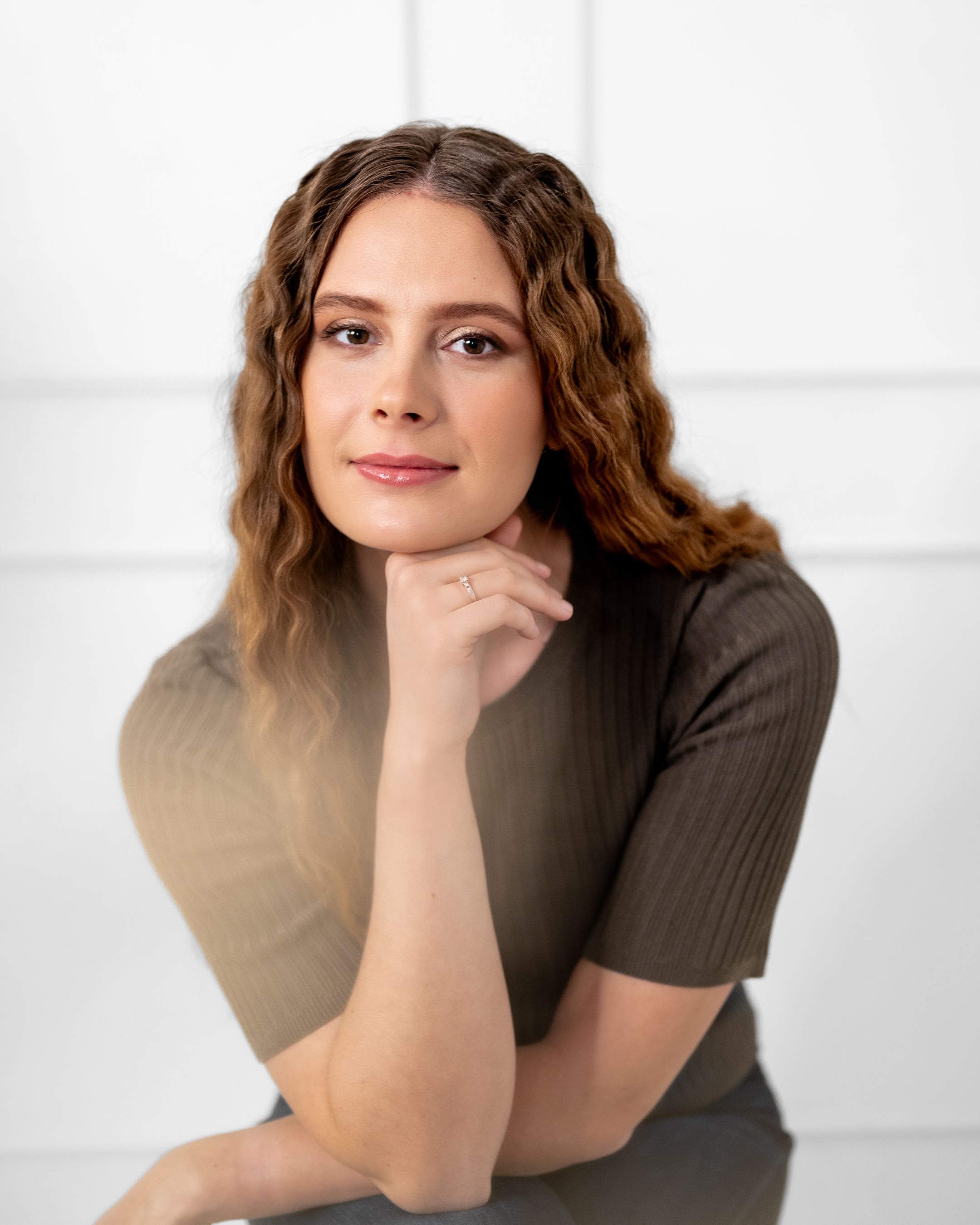Studio portrait with thoughtful pose and gentle smile in brown ribbed top.