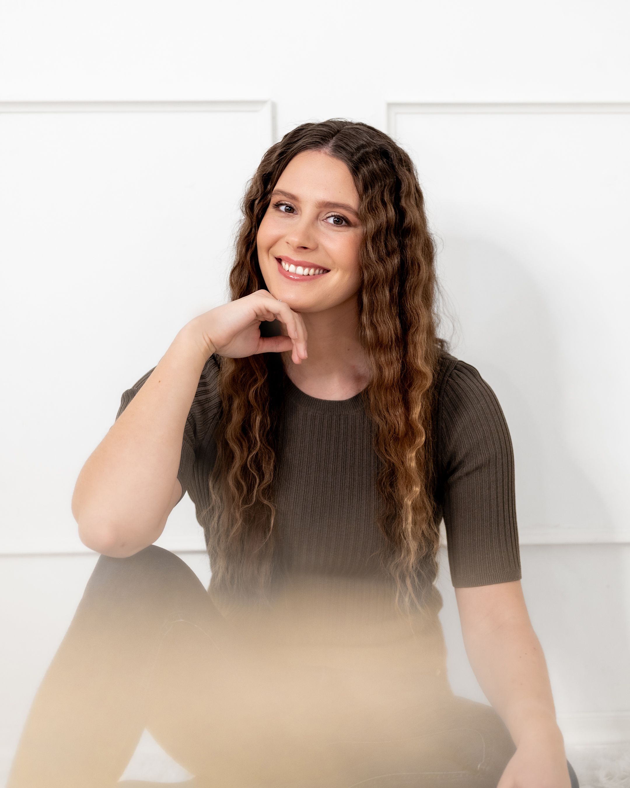Cheerful studio portrait with natural waves and brown top in bright setting.