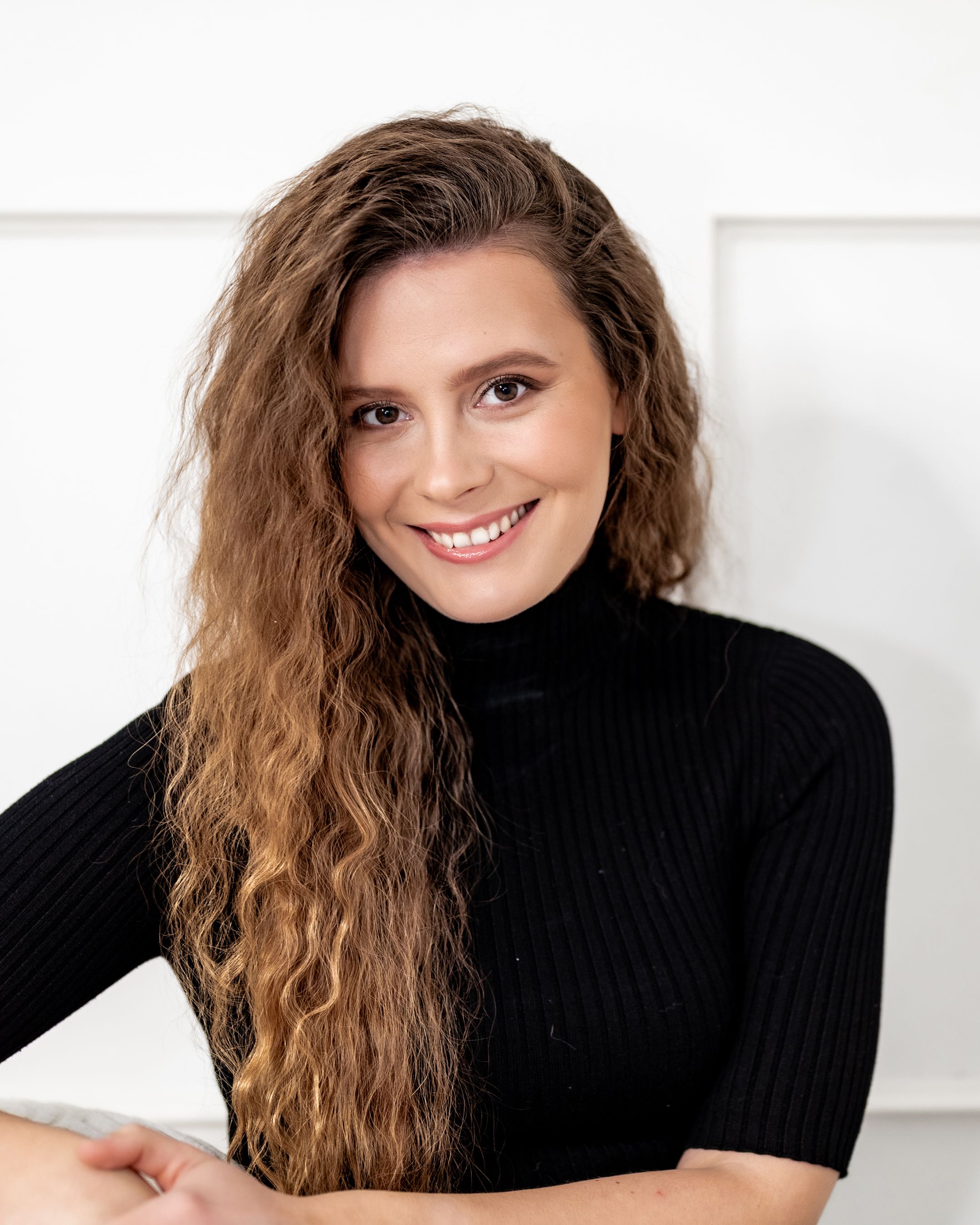 Professional headshot wearing black turtleneck sweater with styled wavy hair.