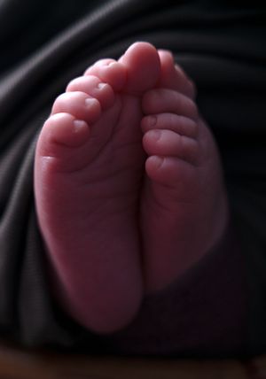 Close-up of soft, tiny newborn baby feet resting on a dark blanket, showcasing delicate toes and smooth skin.