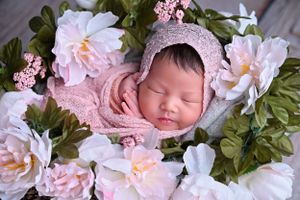 Sleeping newborn baby in pink knit bonnet surrounded by soft pink and white flowers in a cozy basket. best cypress tx newborn photographer