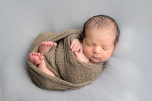 Newborn baby swaddled in a soft gray wrap, peacefully sleeping on a light blue background. affordable cypress tx newborn photographer