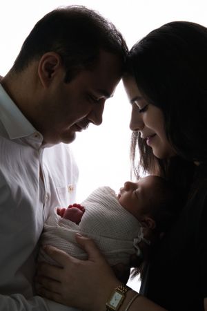 New parents lovingly gaze at their newborn baby wrapped in white, sharing a tender family moment.  cypress baby photography studio