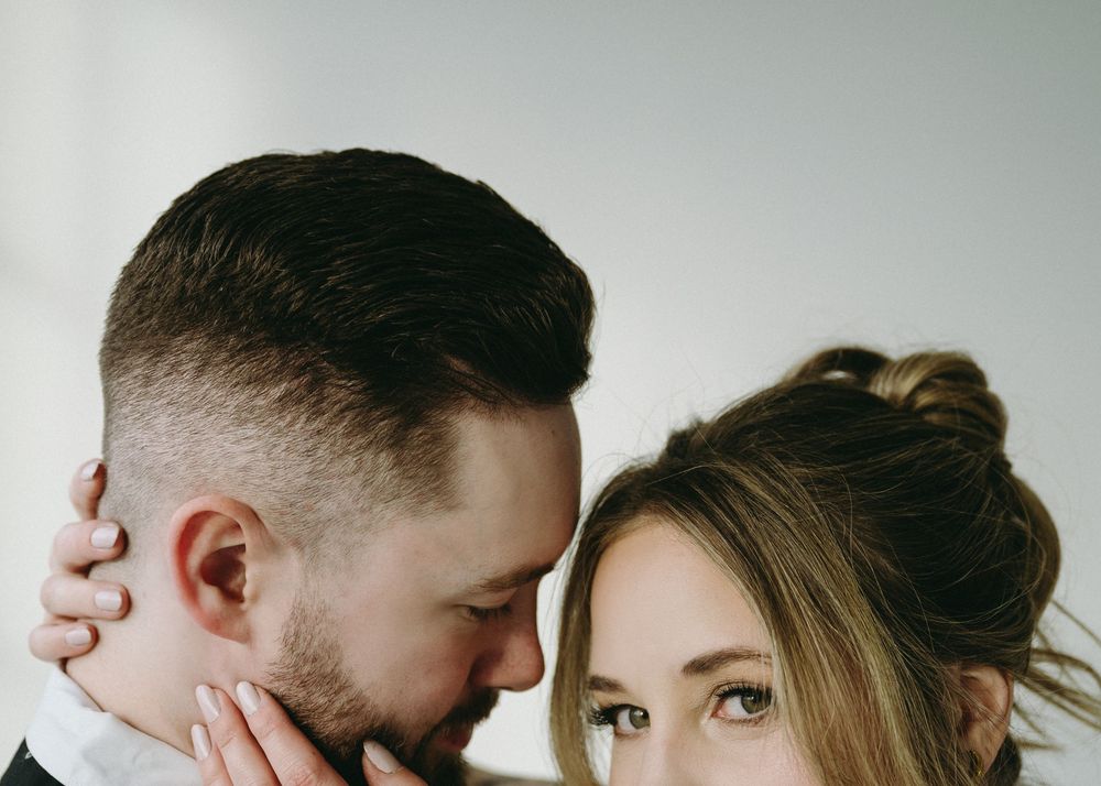 A couple shares an intimate moment against a white background in a minimalist portrait.