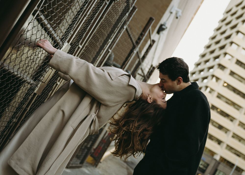 A couple shares a romantic dance pose on an urban street with tall apartment buildings in the background.