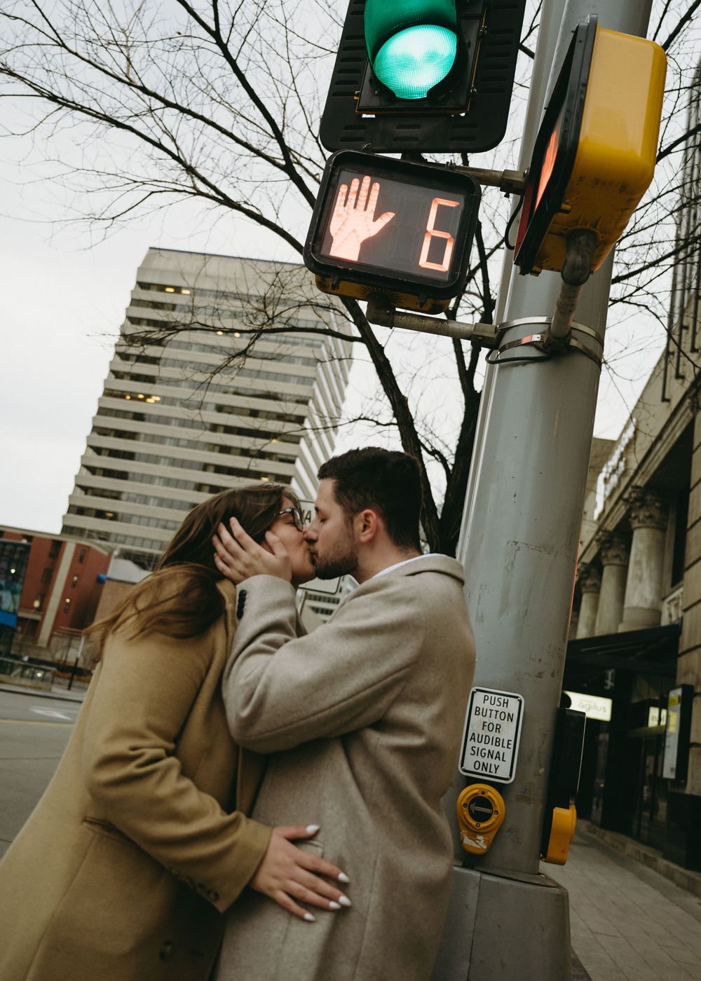A person in a tan coat waves at a traffic light on an empty city street.