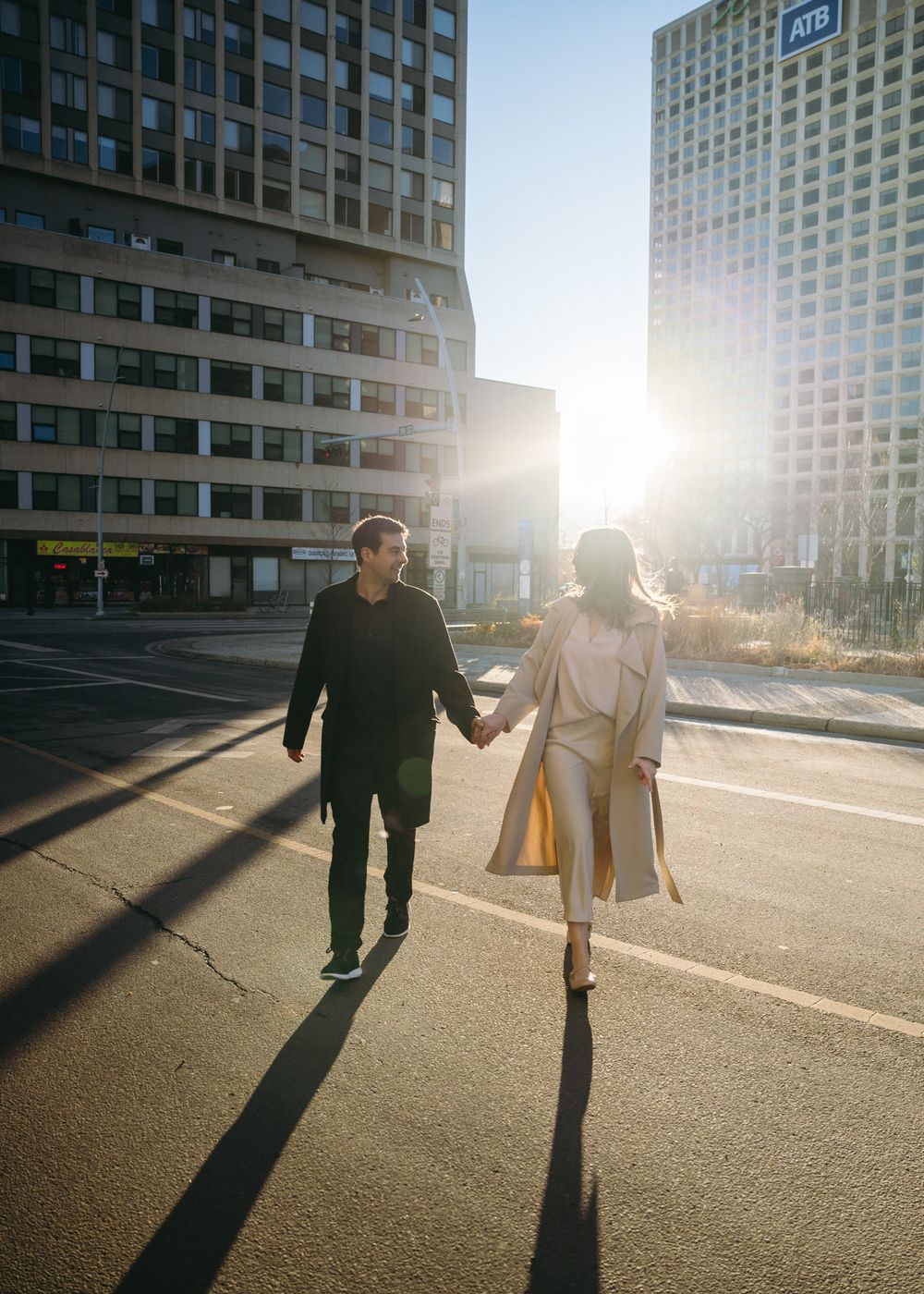 Two people walking together in an urban setting with tall buildings and long shadows cast by sunset lighting.