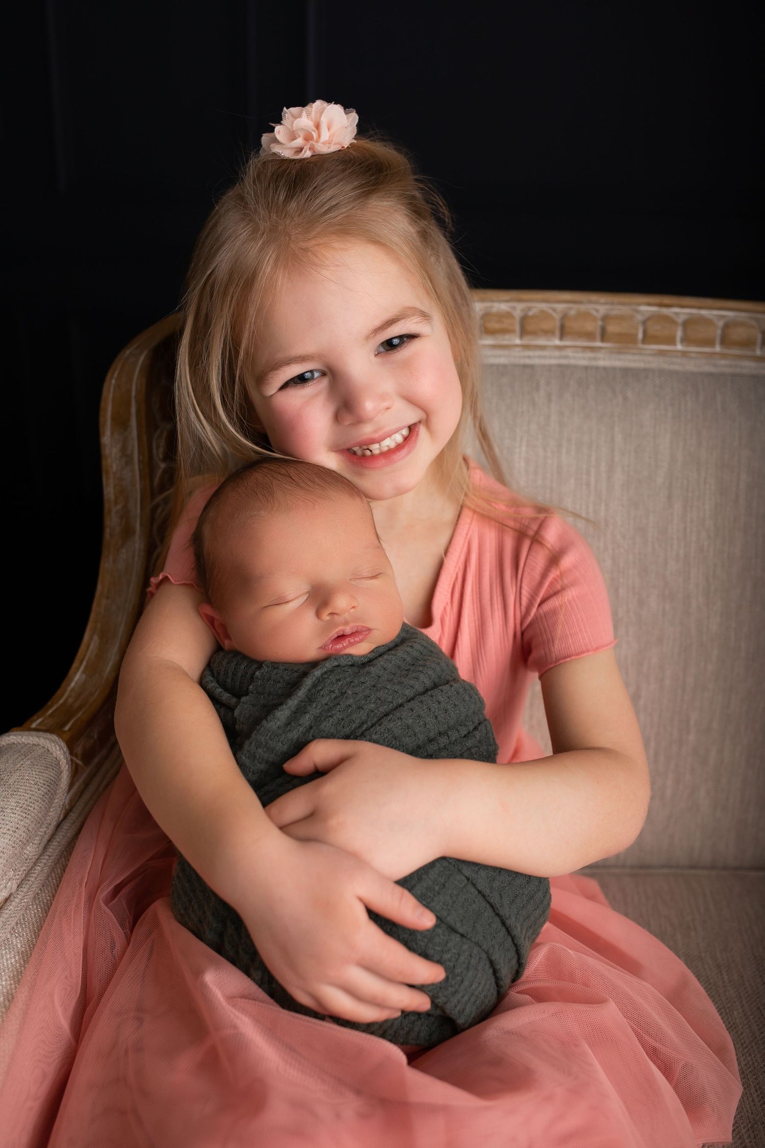 Portrait of siblings on beige chair with soft studio lighting.