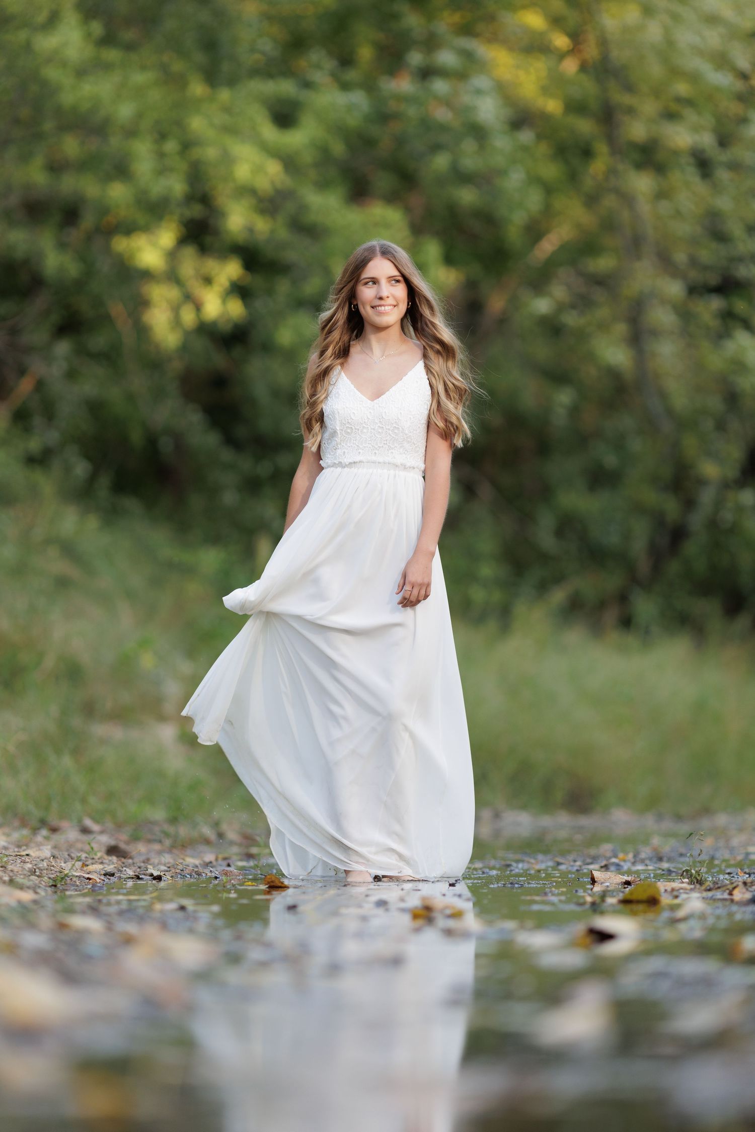 Young lady standing in a shallow creek, wearing a white summer dress.