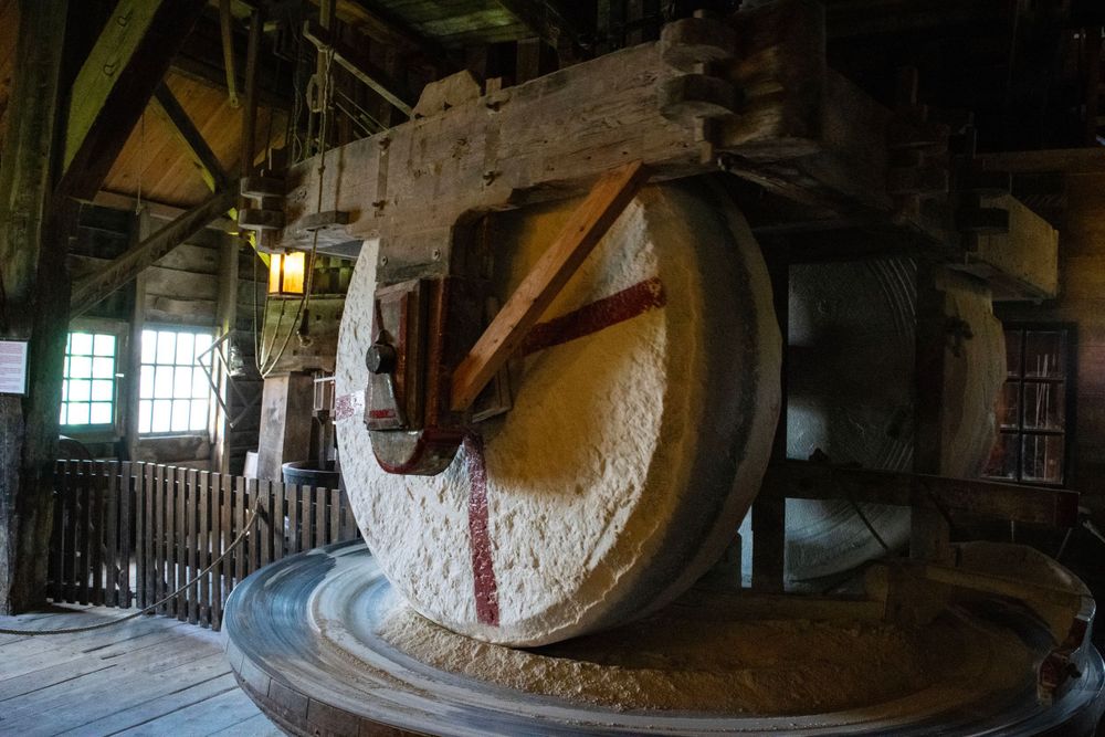 Interior view of an old windmill showing large millstone machinery and wooden beams.