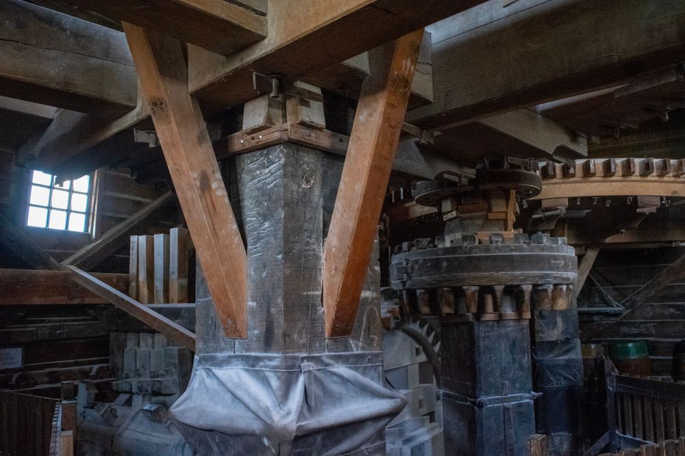 Historic windmill mechanisms with wooden support beams and gears inside an old Dutch mill.