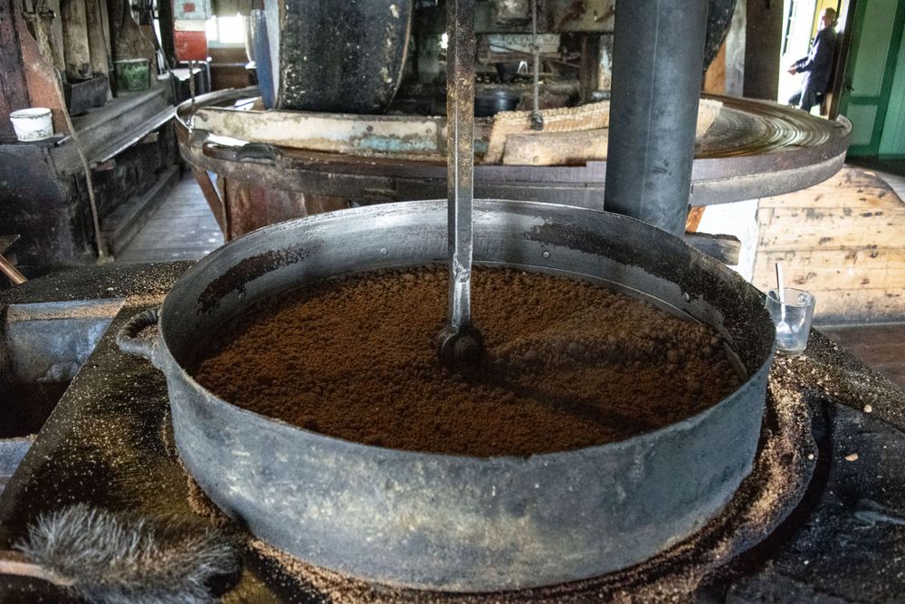 Large circular grinding apparatus filled with brown material inside a traditional windmill.