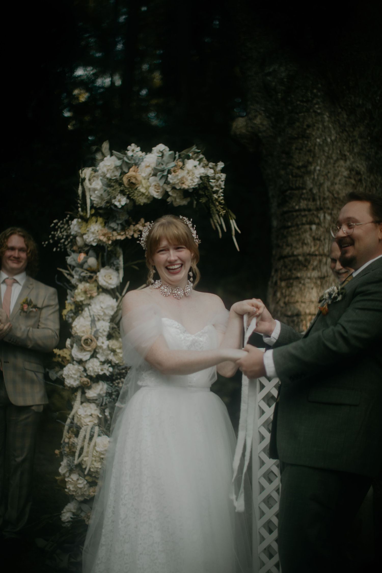 A joyful wedding dance moment captured under a floral arch with guests watching in the background.