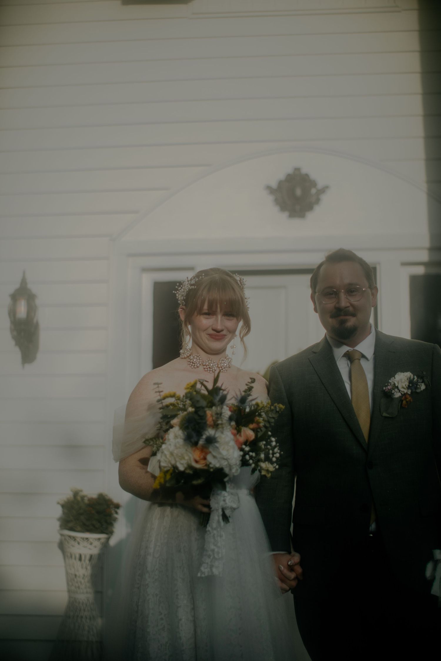 Wedding portrait in front of a classic white building with elegant floral bouquet.