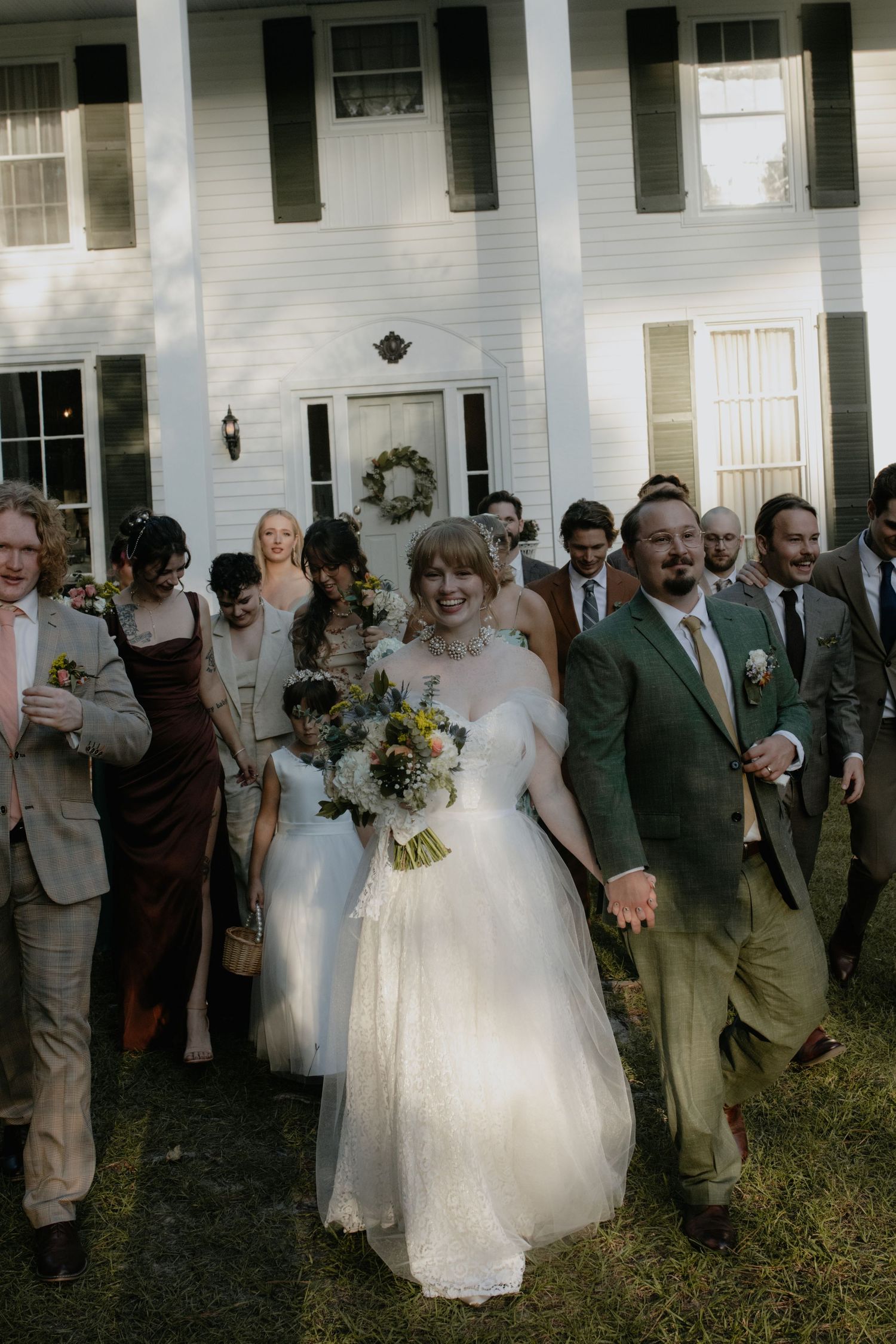 Wedding party and guests gathered for celebratory photo in front of colonial style building.
