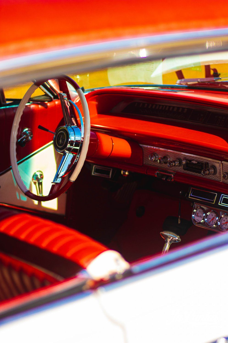Interior view of classic car dashboard and steering wheel in vibrant red tones.