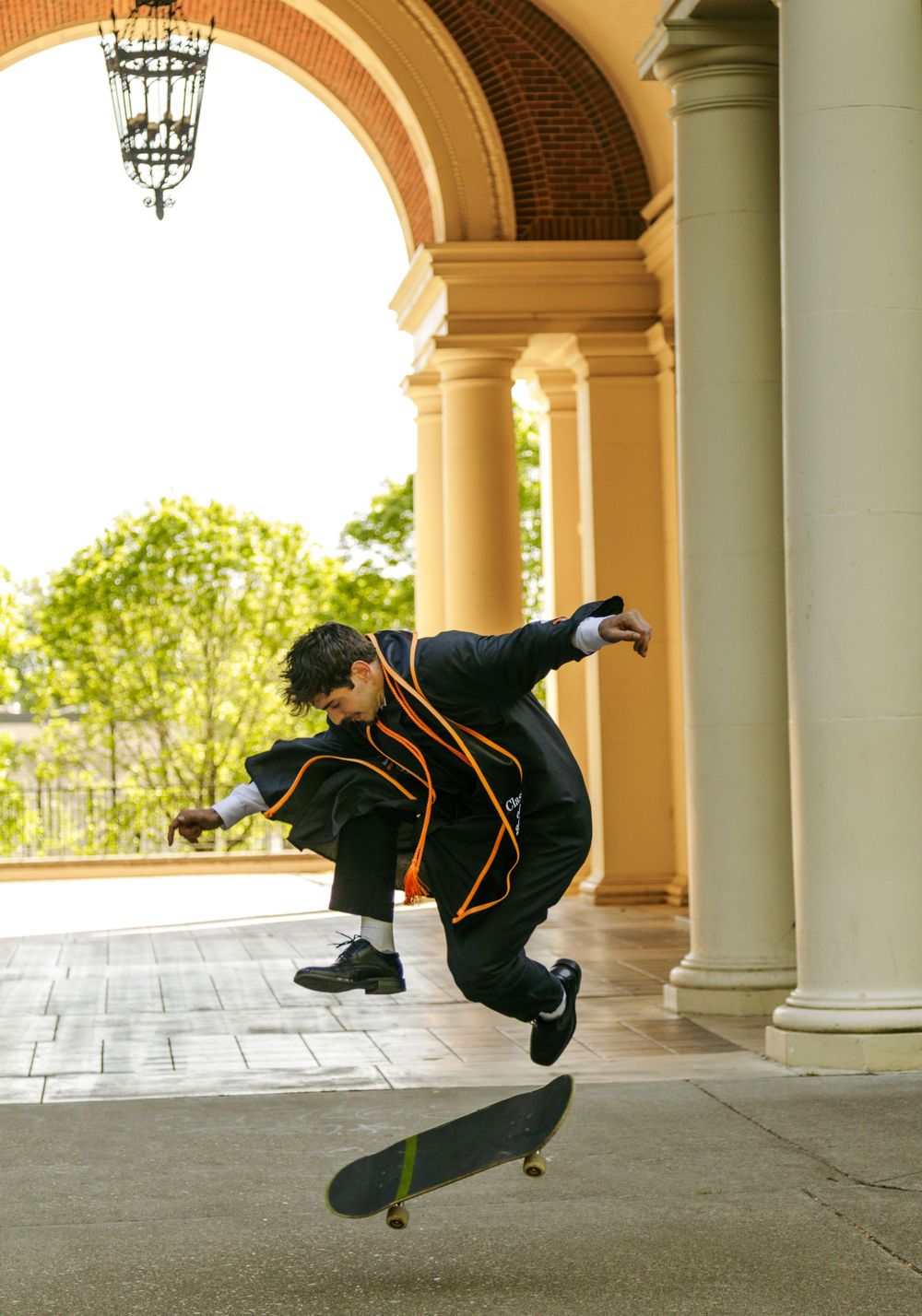 Skateboarder performing a trick mid-air under elegant arched columns of a classical building.