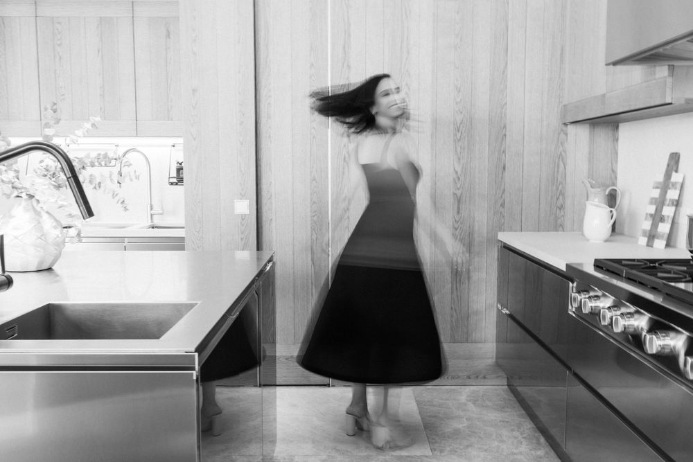 Black and white motion photograph capturing movement in minimalist kitchen interior.