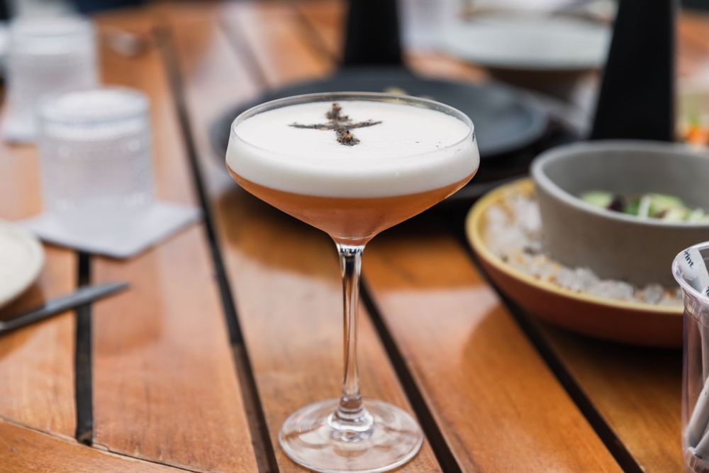 An elegant cocktail with frothy top served in a coupe glass on a wooden table.