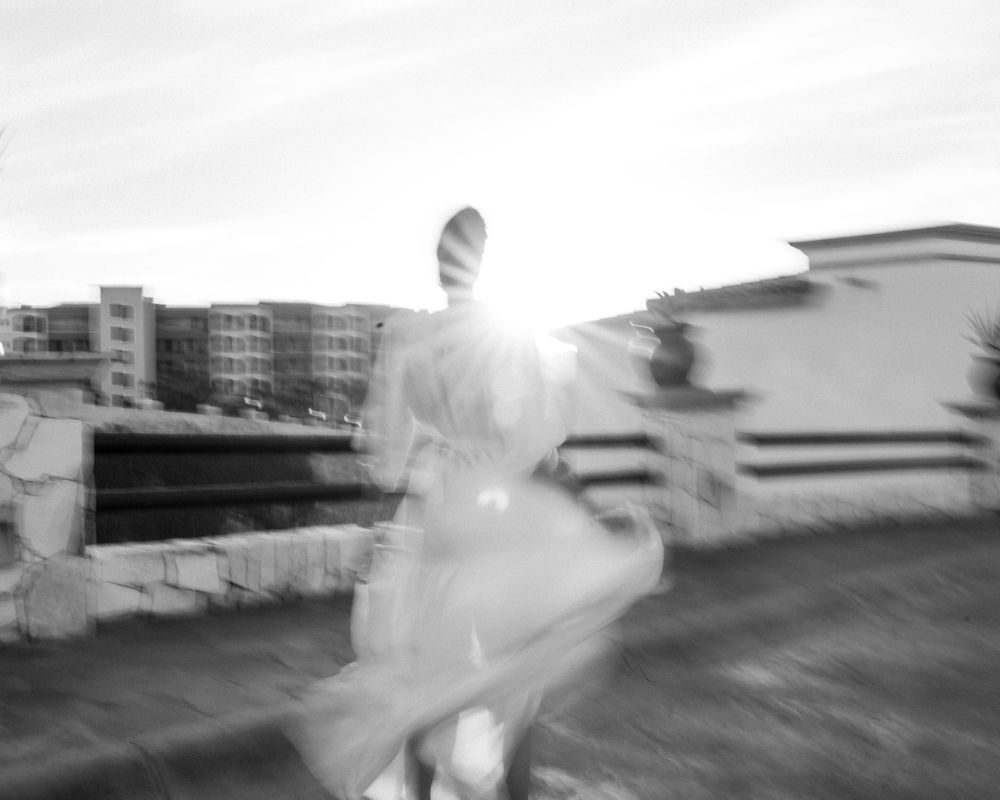 Artistic motion blur photograph of a figure in white dress against urban architecture.
